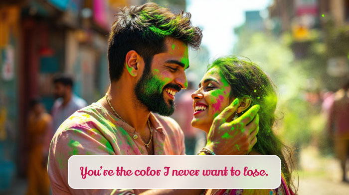 A smiling couple celebrating Holi, as the man playfully applies color to the woman’s face.