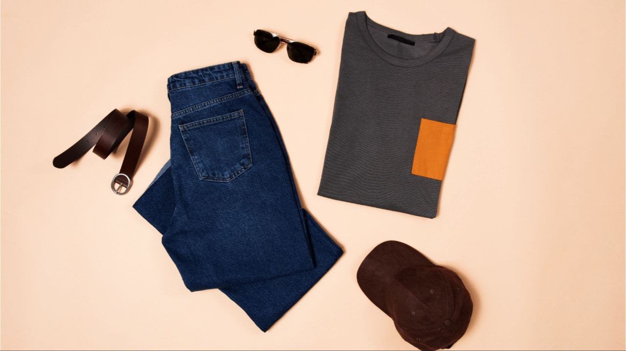 A flat lay shot of a t-shirt, jeans, belt, hat, and a pair of sunglasses.
