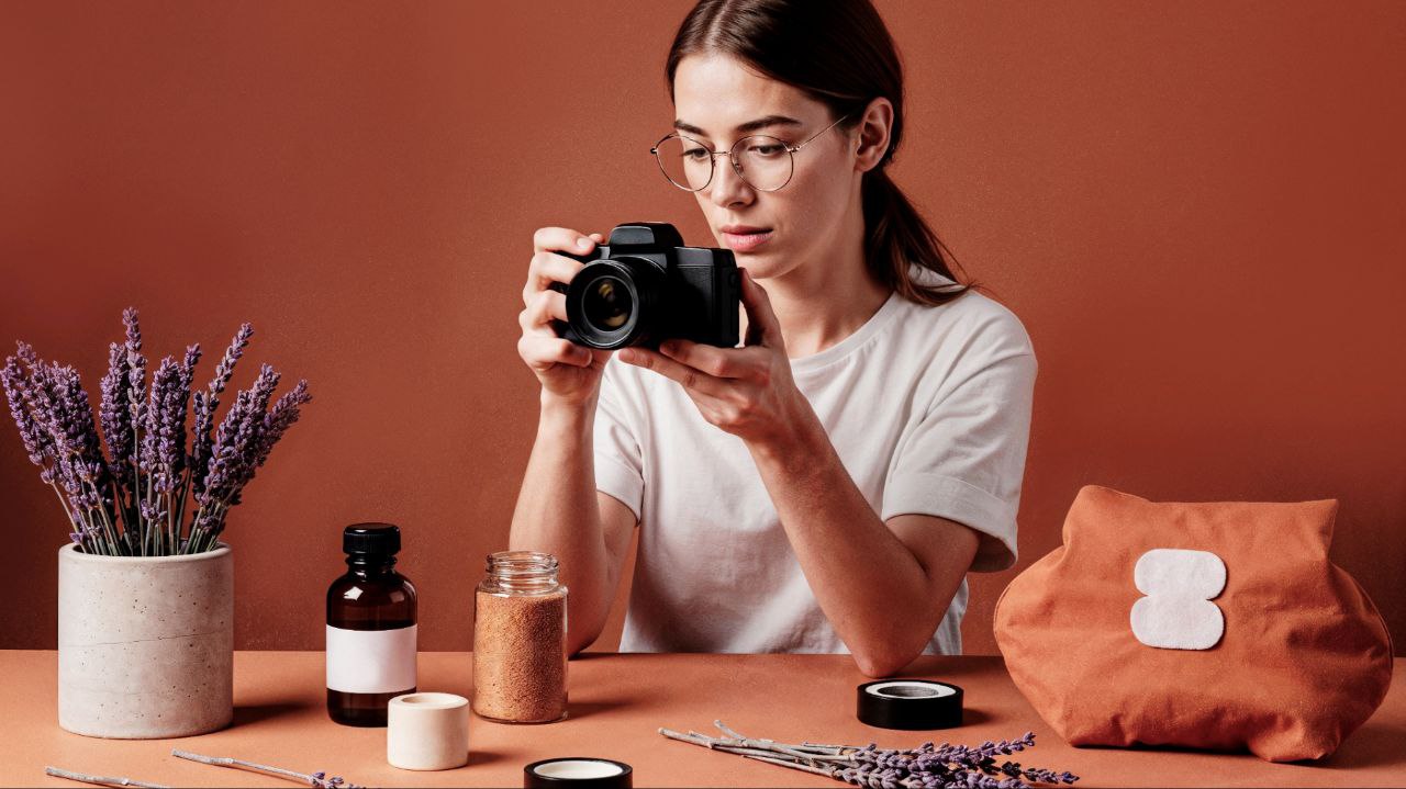 A woman holding a camera and taking pictures of products on a table.